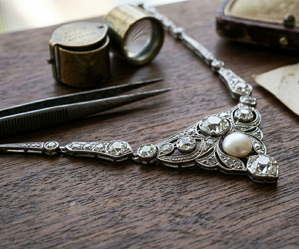 a close-up image of a vintage estate necklace on a wooden table with tweezers and loupe next to it