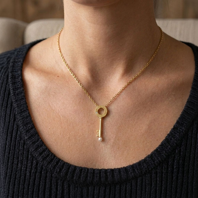 a woman wearing a yellow gold pendant with a key set with a diamond and pearl