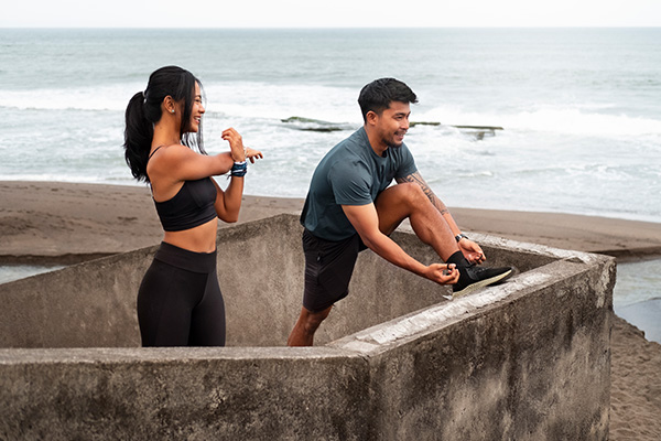 a image of a couple getting ready to workout. They are standing on the stairs of a beach and the man is tying his shoe.