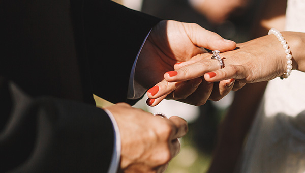 a close-up image of the groom getting ready to put a wedding band on the hand of the bridge