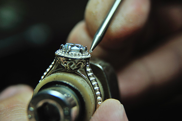 a close up image of a jeweler setting a diamond in a gold ring.