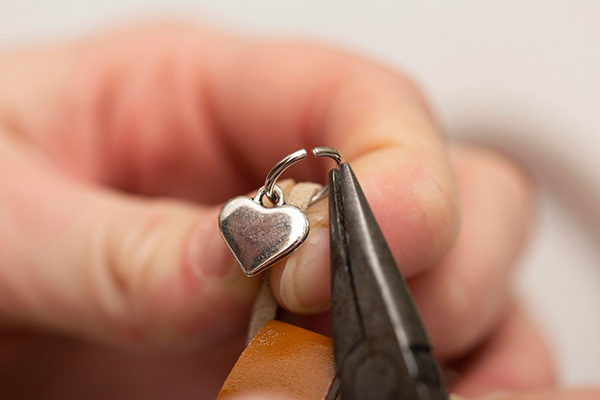 a close up image of a jeweler repairing a silver heart pendant