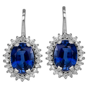 Vintage 18k white gold halo drop earrings set with 4.15 carats of oval blue sapphires and 0.50 carats of round brilliant earth-mined diamonds.