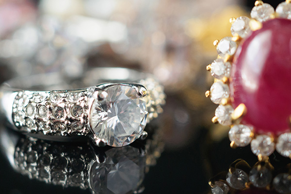 a close up image of a vintage diamond ring next to a red colored gemstone & diamond halo ring.