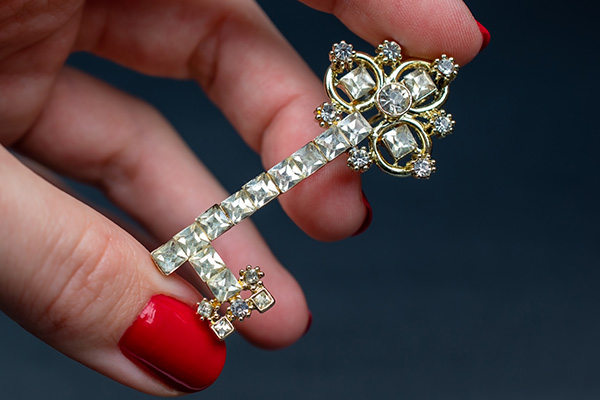 a close up image a of person's hand with red painted nails holding a vintage brooch accented with diamonds.