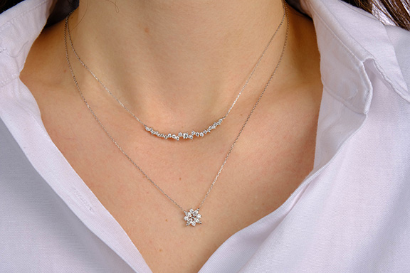 a close up image of a woman wearing stacked diamond pendant necklaces