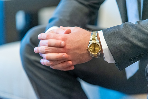 a close up image of a man wearing a rolex on his left wrist. You can see that he is also wearing a suit.